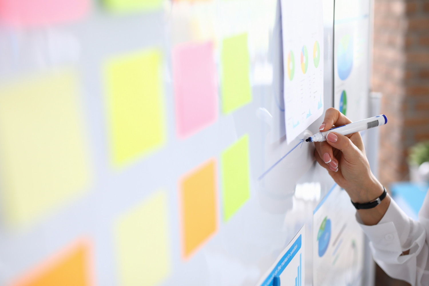A person writes on a whiteboard with colorful sticky notes and printed charts attached to it, mapping out a branding strategy.