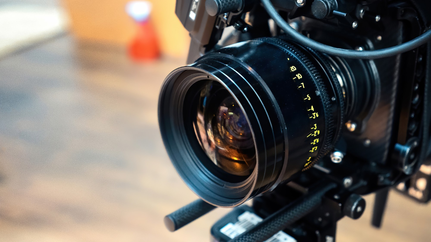 Close-up of a professional video camera lens with focus and aperture markings in yellow, mounted on a rig, ideal for video and photography projects, with a blurred background.