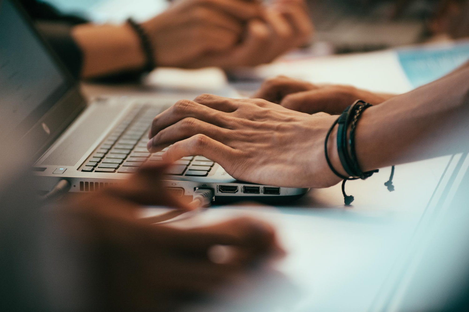 Close-up of hands typing on a laptop keyboard, with other people’s hands and arms visible in the background—perfect for illustrating teamwork in SEO or collaborative Search Engine Optimisation projects.