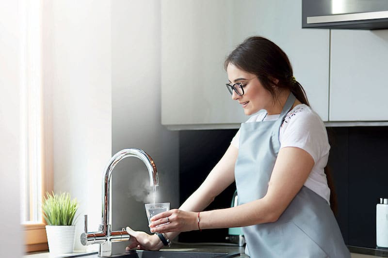 A woman in an apron washing dishes in a home kitchen.