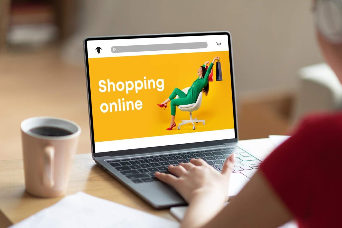 A person uses a laptop displaying an online shopping website with "Shopping online" text and a "Buy now" button. An image of a woman holding shopping bags pops against the yellow background, highlighting the psychology behind digital retail therapy. A coffee cup sits nearby.