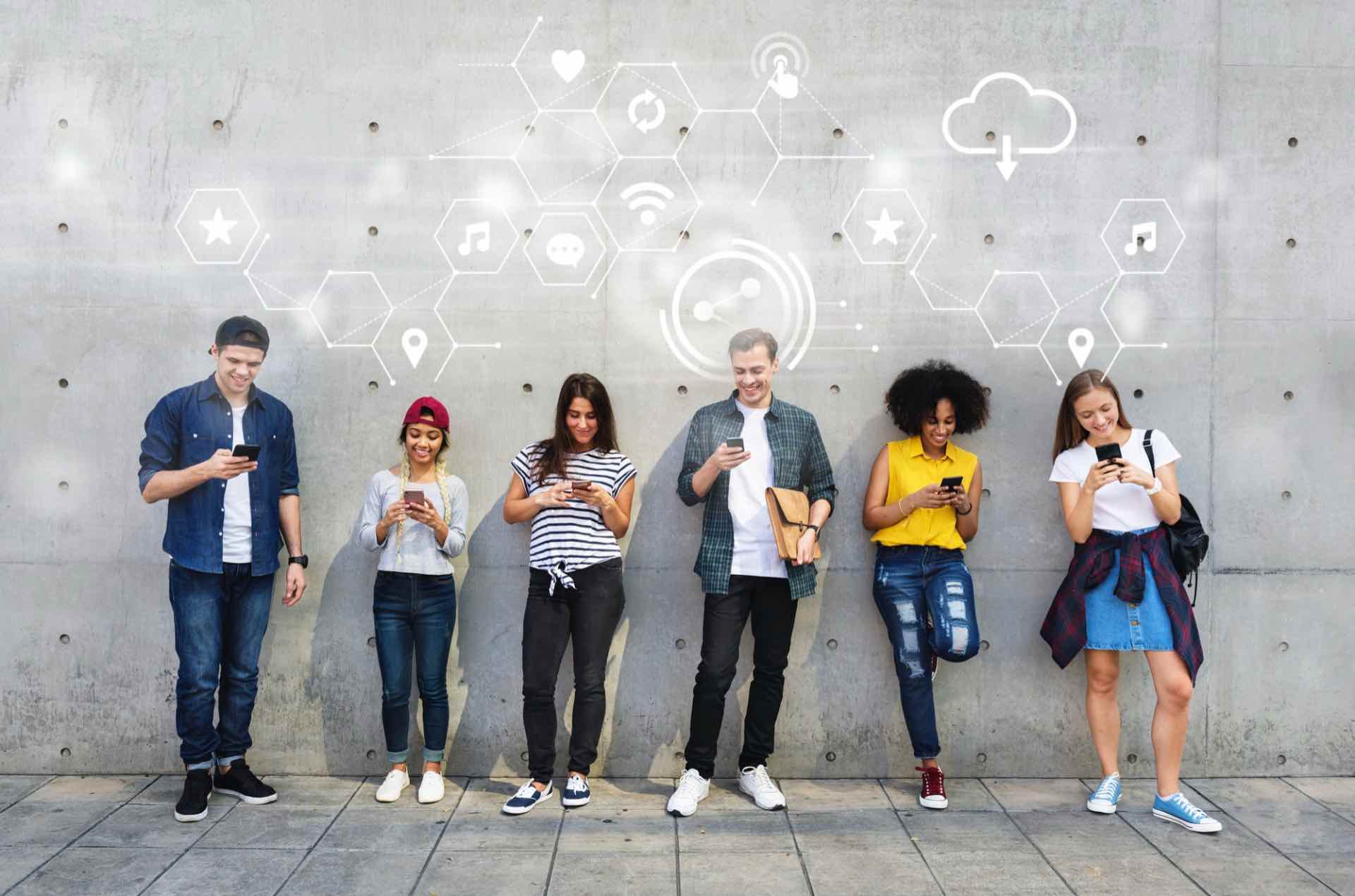 Six young adults stand against a concrete wall, each looking at their smartphones, with digital icons representing social media content and connectivity displayed above their heads.
